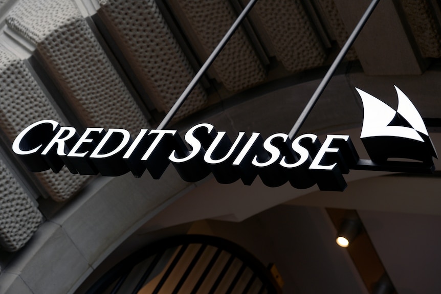 The Credit Suisse logo, which are the words in white on a shiny black building wall.
