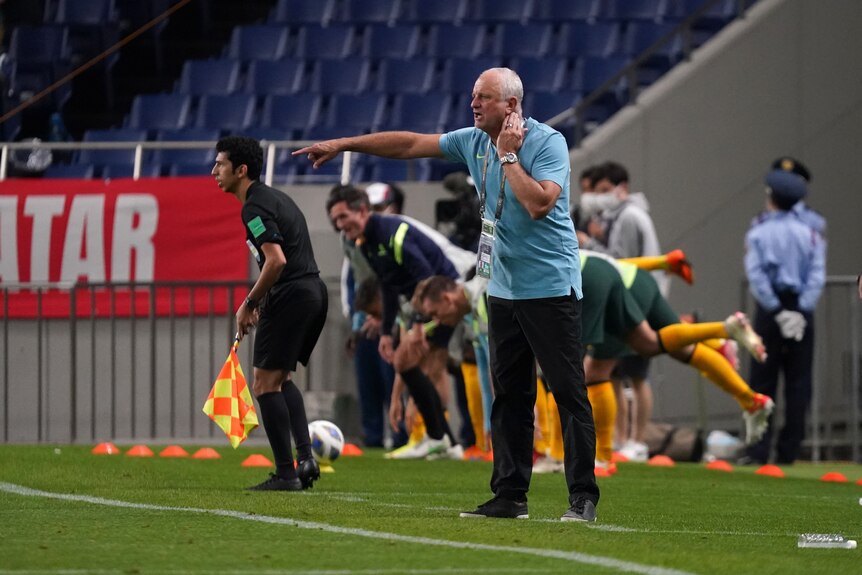 Socceroos coach Graham Arnold stands on the sideline, calling out to players and gesticulating during a World Cup qualifier. 