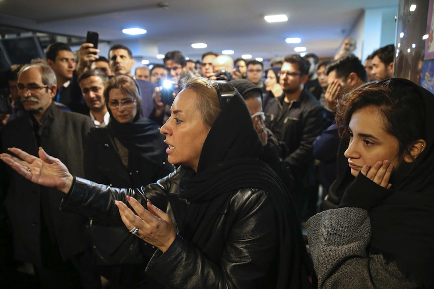 Medium shot of a crowd with a woman at the front gesturing.