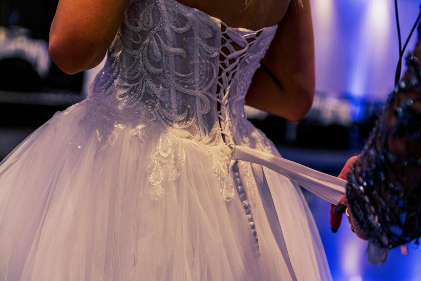 A close-up of a pair of hands tying ribbons on the back of a formal dress.