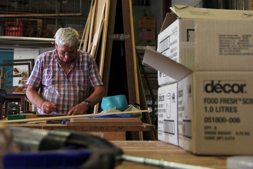 Retired carpenter David Taylor at a workshop desk, making marks with a ruler.