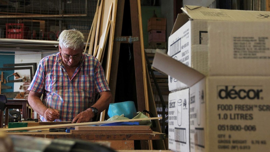 Retired carpenter David Taylor at a workshop desk, making marks with a ruler.