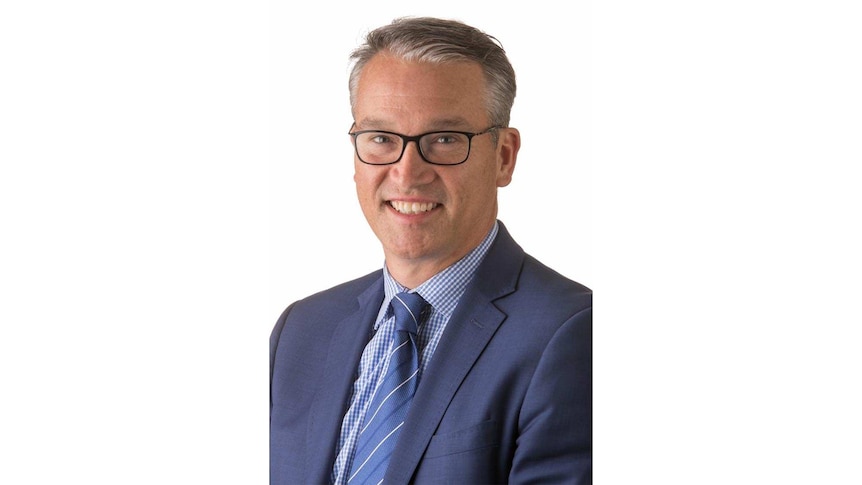 A man in a blue suit and glasses smiling