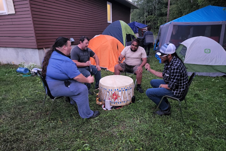 four men sit around a big drum.