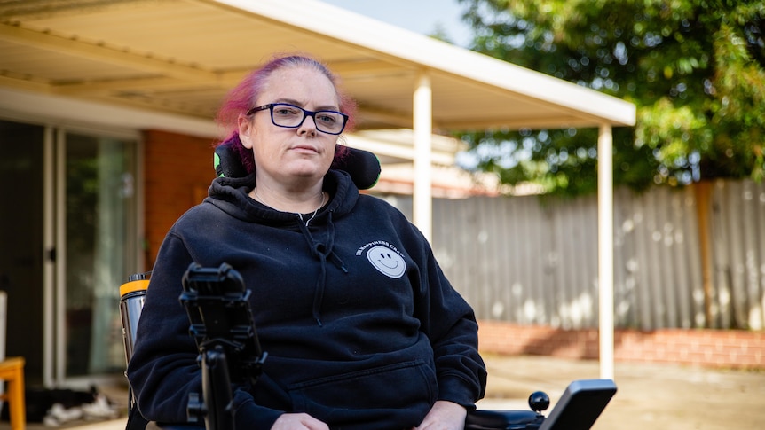 A woman looking serious in her wheelchair in a suburban backyard.