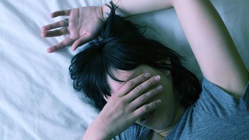 Young woman lying in bed with her arm over her face trying to get to sleep.