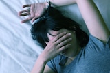 Young woman lying in bed with her arm over her face trying to get to sleep.