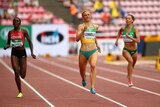 A female sprinter wearing green and yellow runs along a track