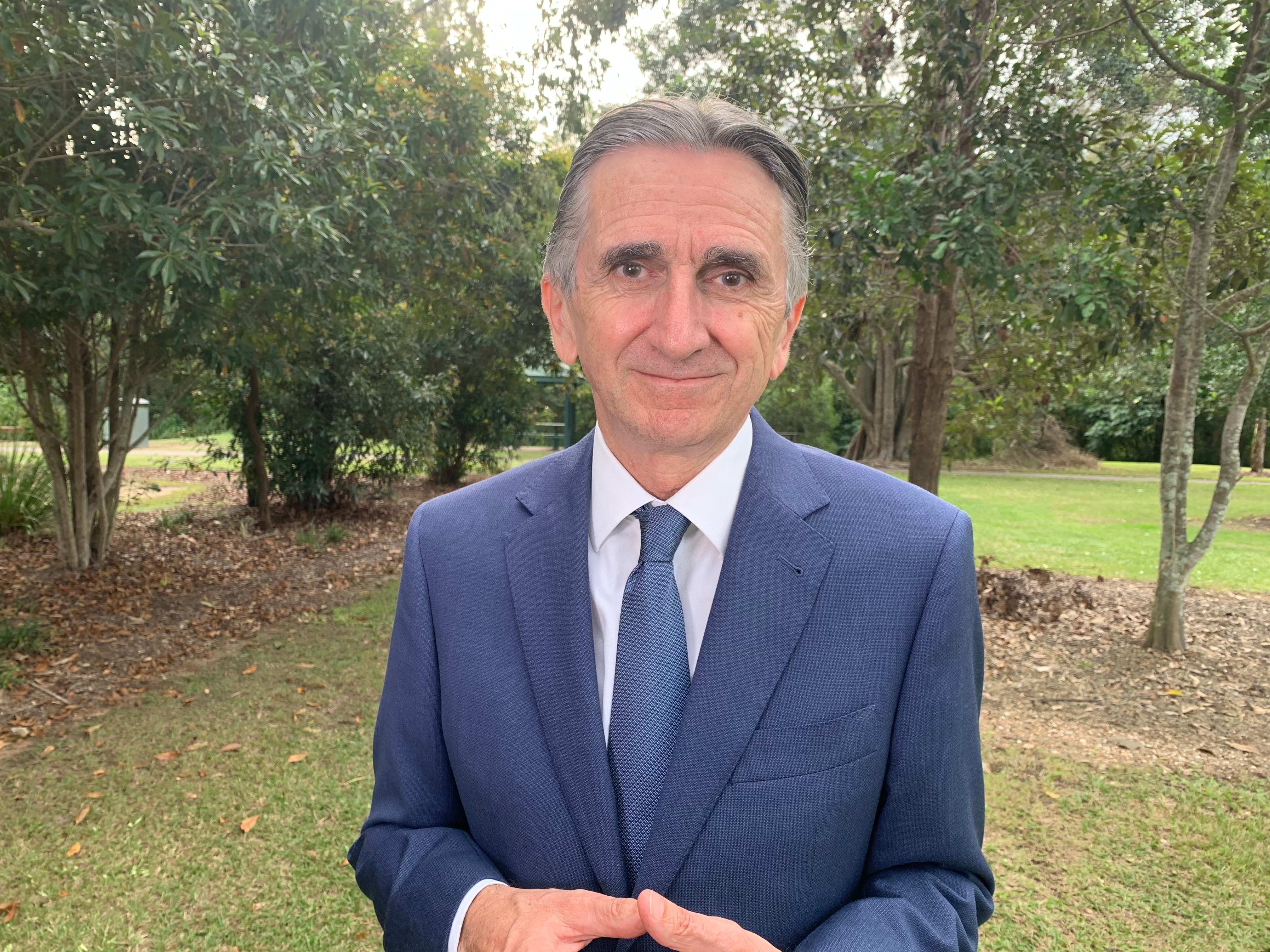 Man in blue suit and tie stands among trees