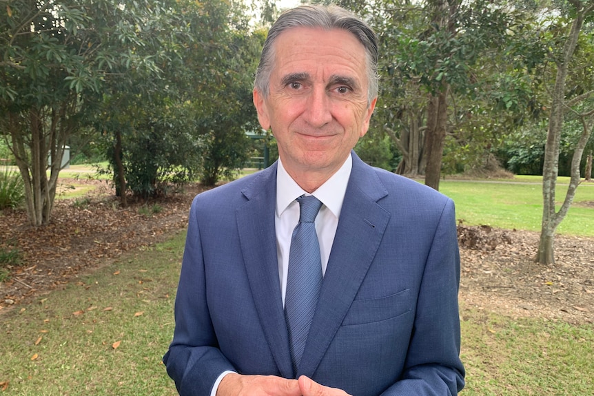 Man in blue suit and tie stands among trees