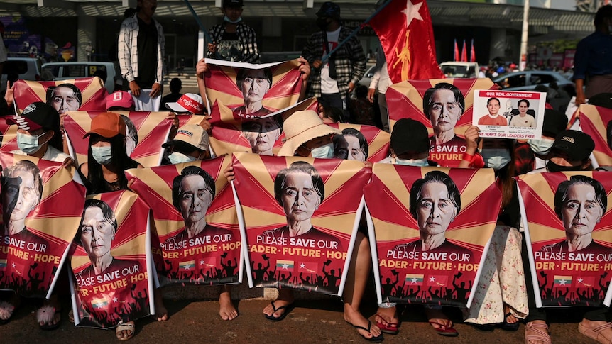 Myanmar protesters hold red posters with Aung San Suu Kyi's face on them.