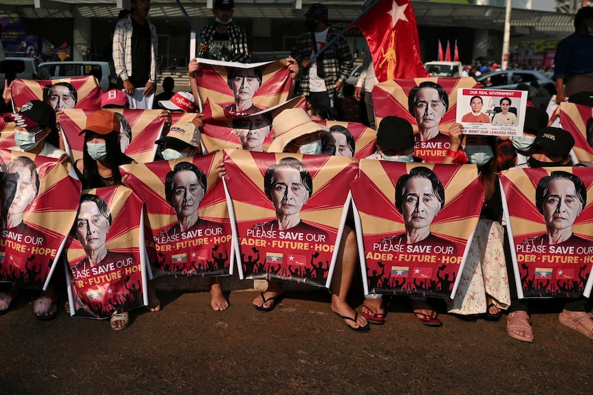 Myanmar protesters hold red posters with Aung San Suu Kyi's face on them.