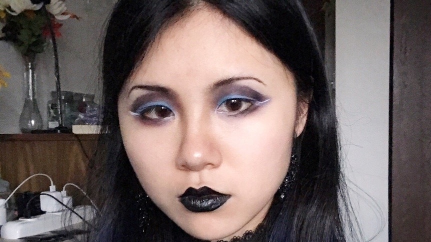 A Chinese woman wearing black clothing and black make-up takes a selfie.