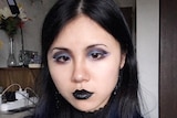 A Chinese woman wearing black clothing and black make-up takes a selfie.