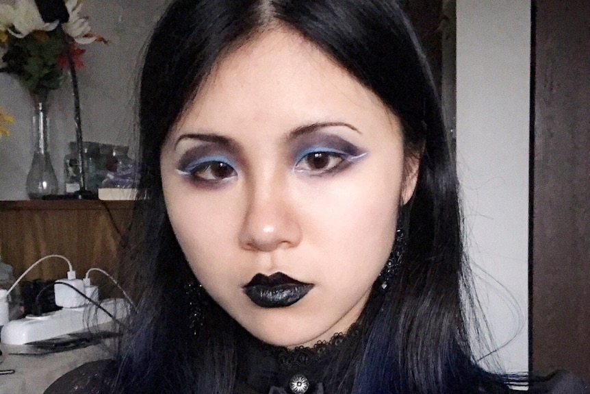 A Chinese woman wearing black clothing and black make-up takes a selfie.