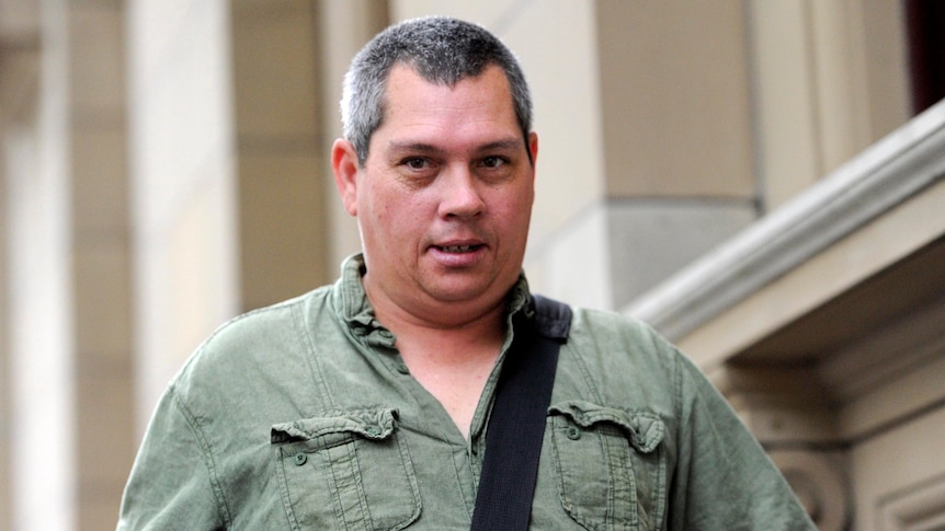 Brendan Sokaluk, a man wearing a khaki-green shirt and carrying a bag over one shoulder, looks past the camera.