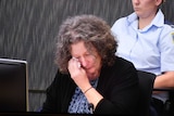 A woman wearing a black cardigan sitting down wipes her eyes.
