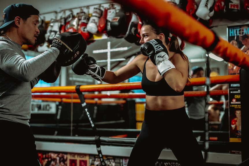 Skye Nicolson hitting pads with a trainer in a boxing arena.
