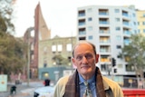 Balding man in front of burnt building on city street