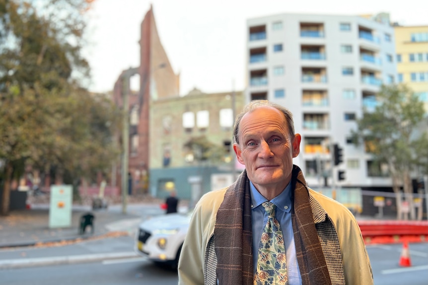 Balding man in front of burnt building on city street