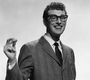 Buddy Holly publicity picture for Brunswick Records. He wears a suit, tie and glasses and clicks his fingers.