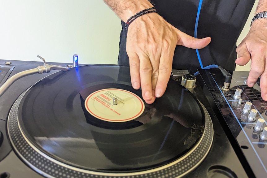A close up of Andrew's olive-skinned hand playing a vinyl on a turntable