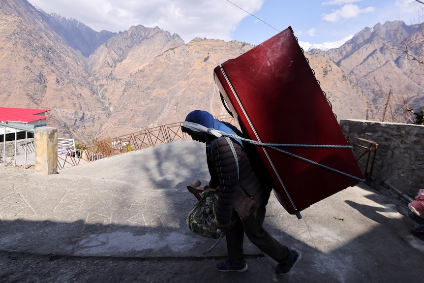 在一张背着冰箱的男人的照片中，他正把它带到某个地方。 背景是山脉。