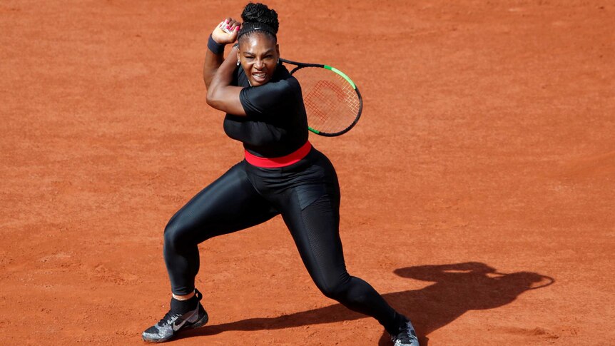 Serena Williams swings her racket over her shoulder, behind her back, half crouched, wearing a skin-tight black suit.