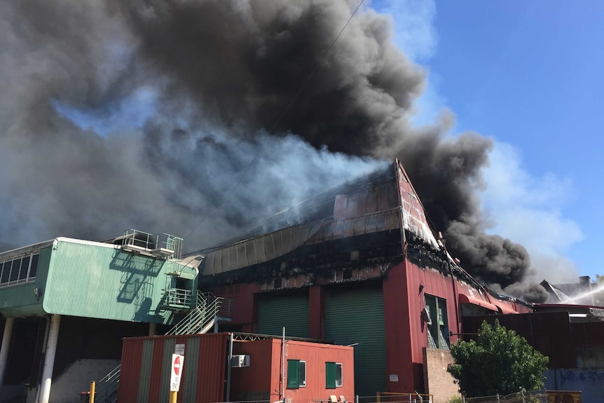 A large plume of smoke rises over a partially collapsed brick building.