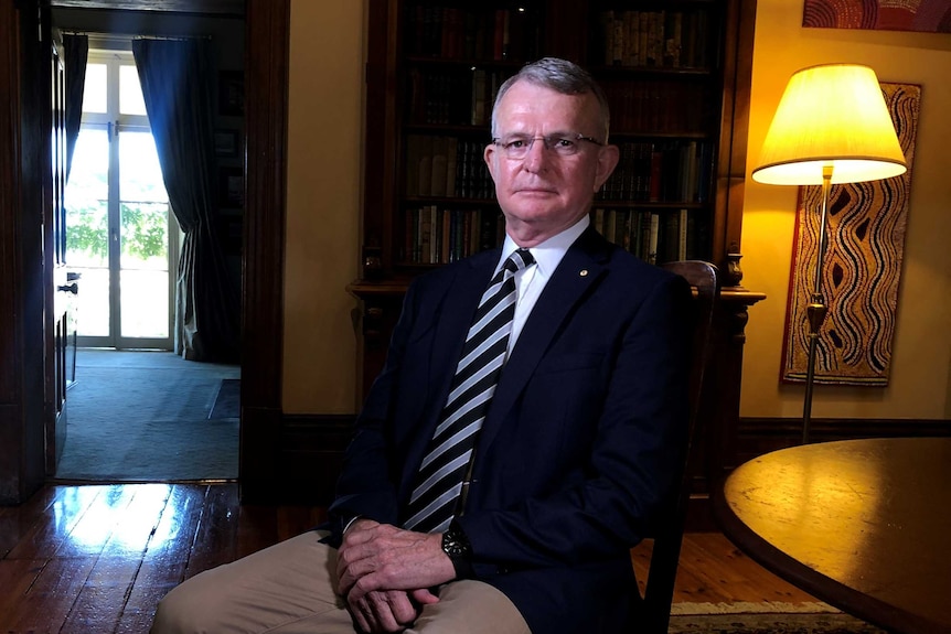 A man in a jacket and tie sitting inside an old, dark house