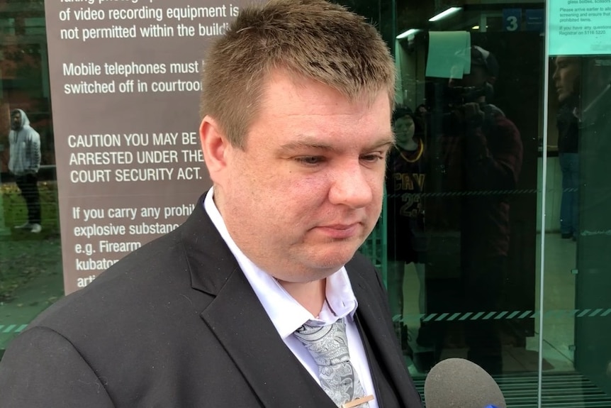 A man with short hair and a suit jacket talking into a microphone.