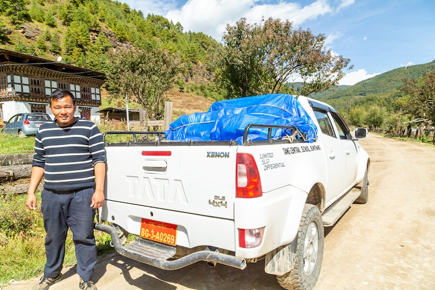 A Bhutanese man stands next to a vehicle with a supply of books in the back.