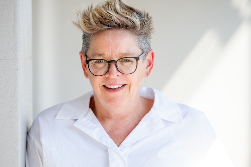 A woman with blonde hair and black rimmed spectacles poses for a photo.