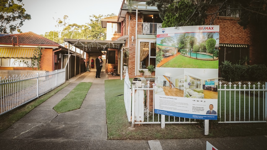 A house with a for sale sign out the front and people out the front