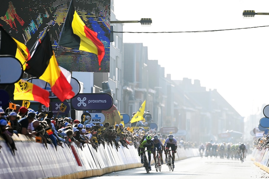 Un groupe de cyclistes sprinte sous des drapeaux avec un autre groupe en arrière-plan
