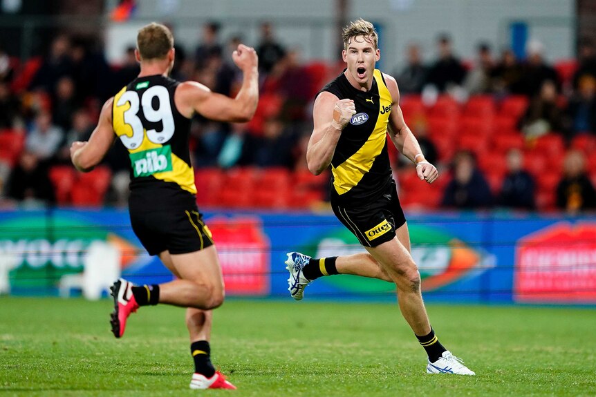 A Richmond Tigers AFL player pumps his right fist as he runs towards a teammate after kicking a goal.