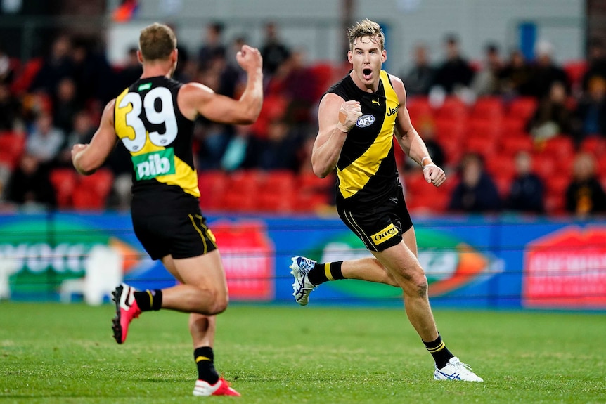 A Richmond Tigers AFL player pumps his right fist as he runs towards a teammate after kicking a goal.