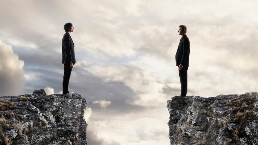 two men in suits looks across at each divided by a deep chasm 