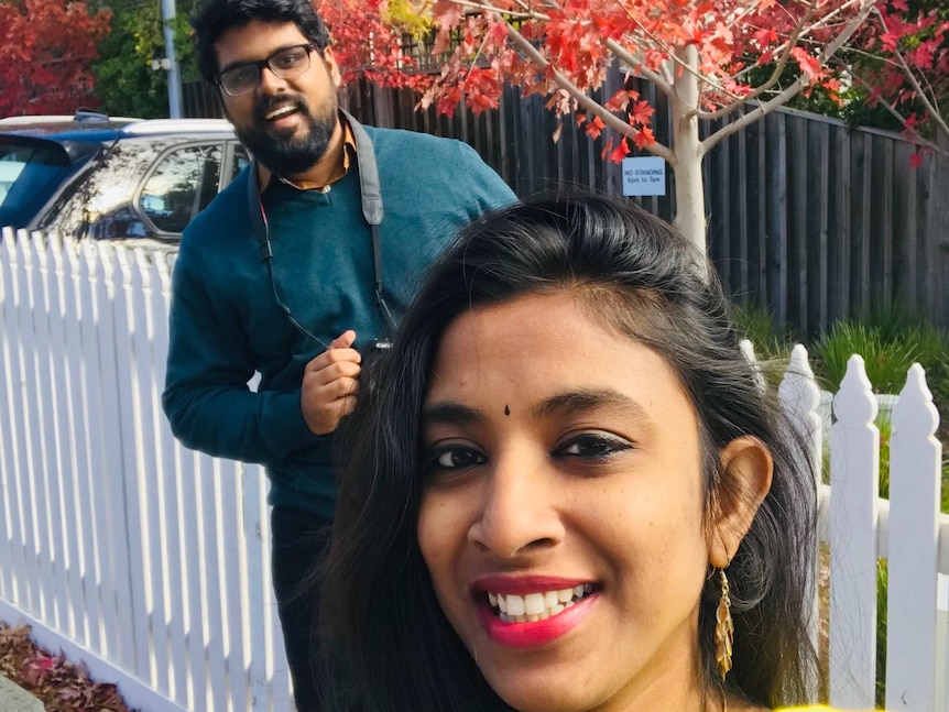 Two people pose in front of a tree