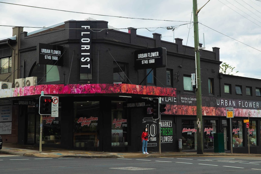 A corner facade charcoal with pink flowers, a person waits at the lights