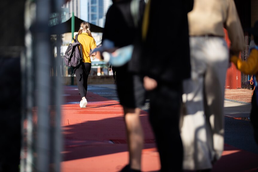 School girl in yellow shirt with bag walking.