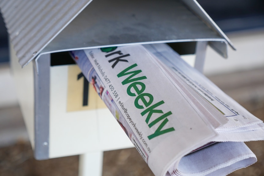 A newspaper sits in a letterbox. 