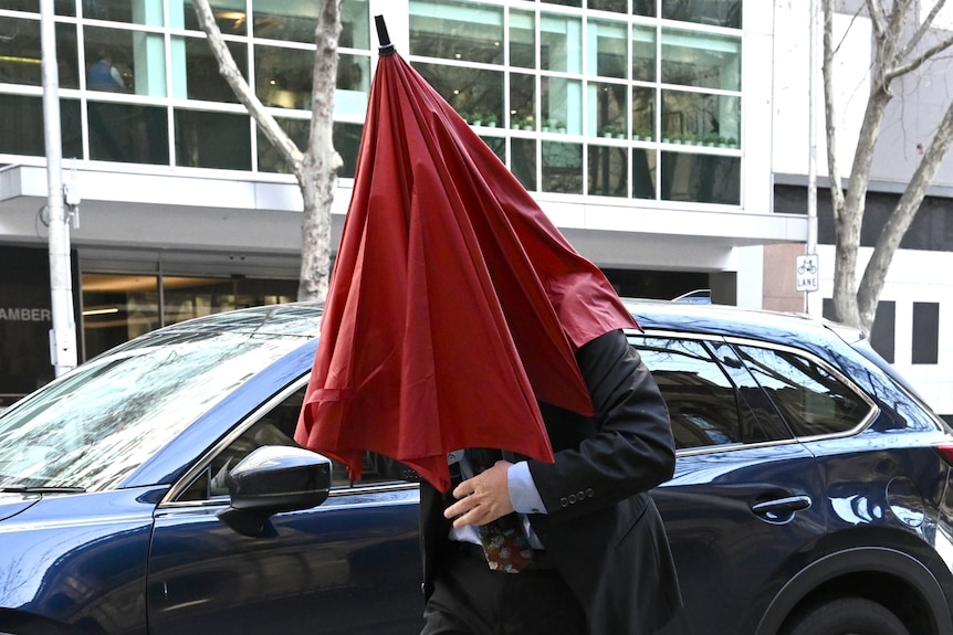 Man in suit covering his top half with a red umbrella 