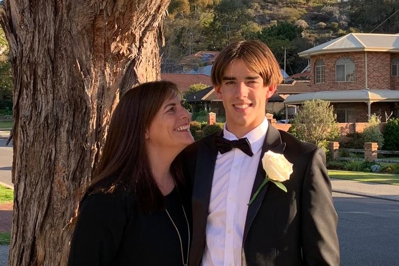 Woman stands next to young man in formal attire, smiling