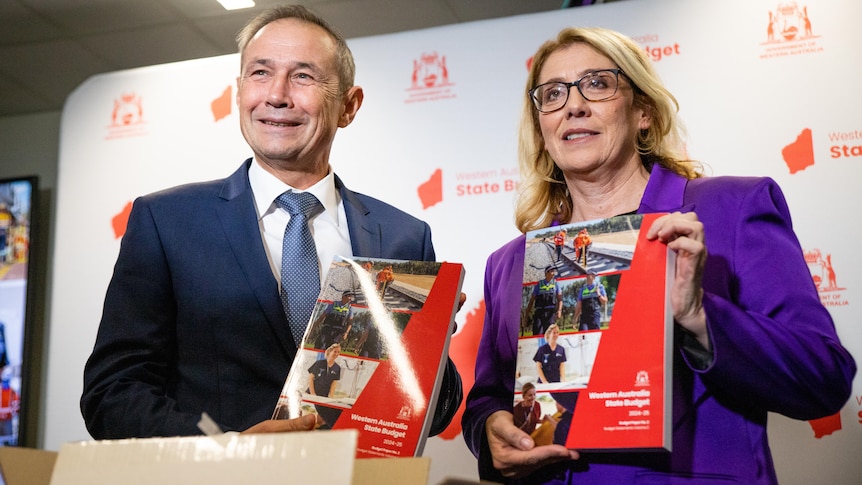 WA Premier Roger Cook and Rita Saffioti stand posing with budget papers while smiling broadly