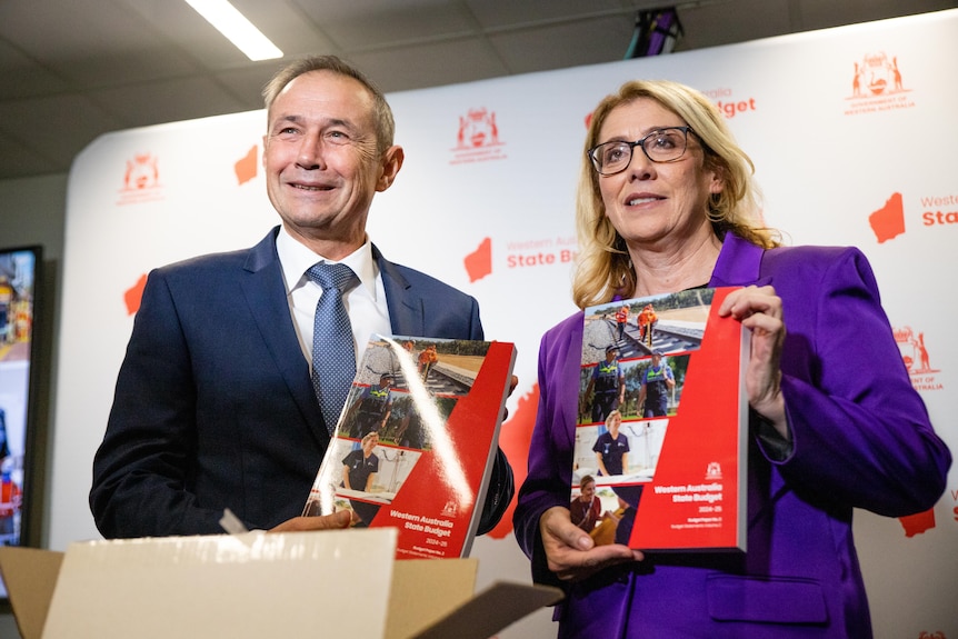 WA Premier Roger Cook and Rita Saffioti stand posing with budget papers while smiling broadly