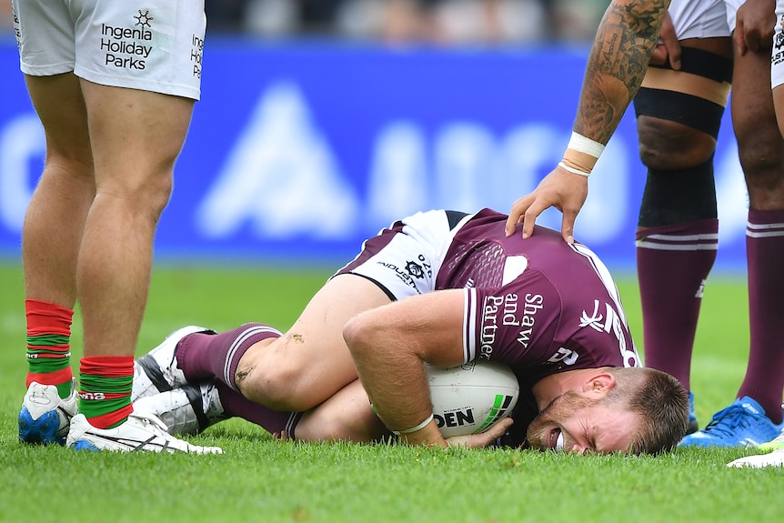 A man lies on the ground in pain clutching a football