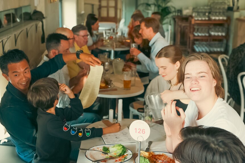 A group of children and middle aged people eat a meal and drink at a Melbourne pub.