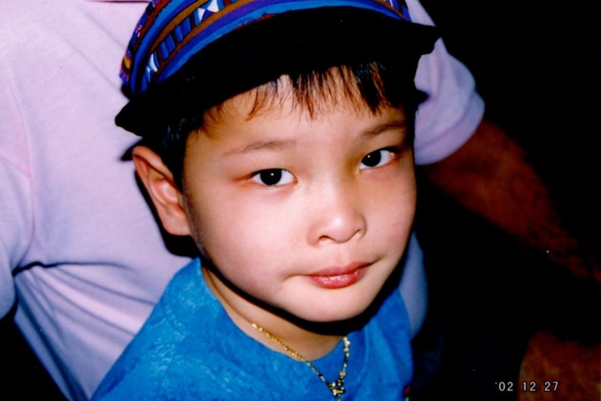 An Asian child looks to the camera with searching eyes and a neutral expression. He wears a cap and is seen from chest-up.