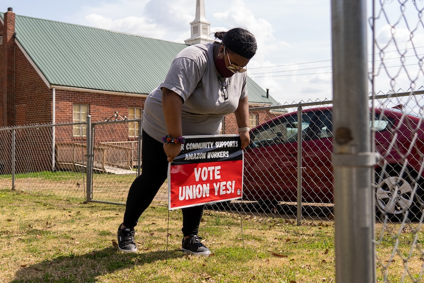 A woman stakes a pro-union yard sign into grass behind a fence 